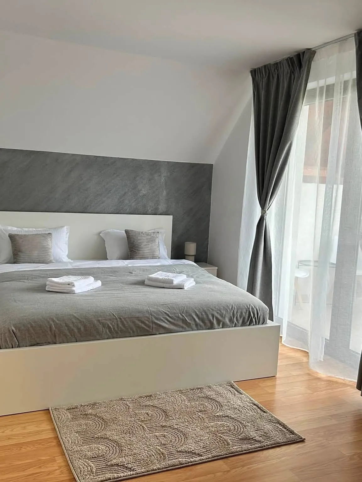 Un dormitor din Vila Safir, cu pat dublu, lenjerie gri și prosoape pregătite, cu ușă spre balcon
